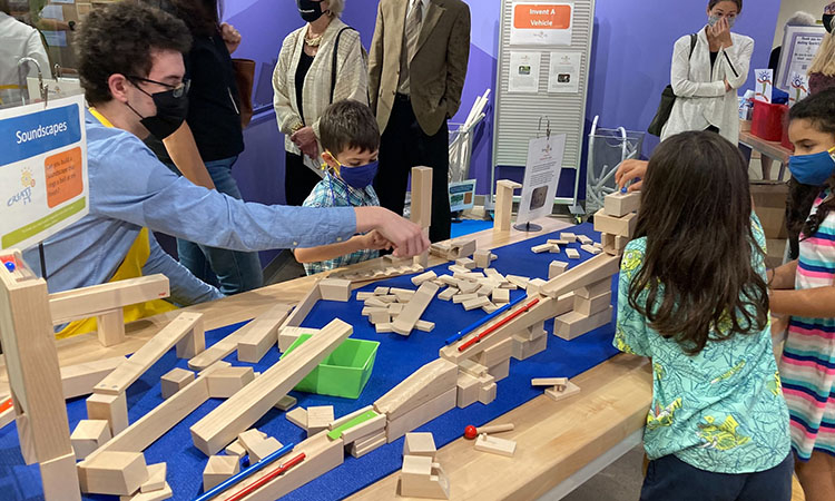 2 young girls, a young boy, and an adult man link wooden ramps together to build a marble run