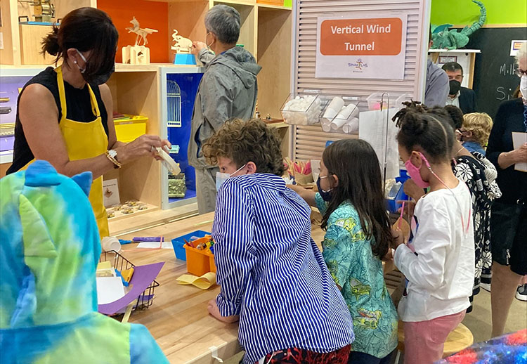 A group of children and a woman facilitator at a table strewn with craft materials