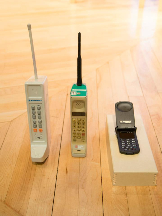 Two early Motorola “brick” phones and an early flip phone.