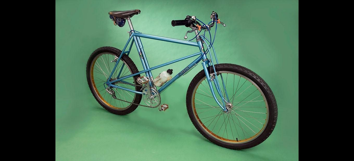Blue mountain bike photographed in profile against a green background