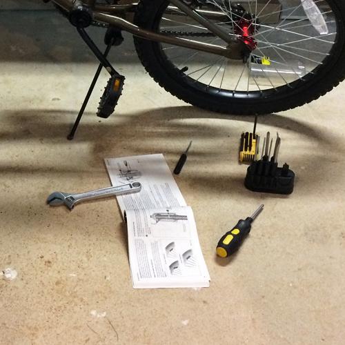 The author has set out the tools and instructions needed to repair his son’s bike on the garage floor in front of the bike