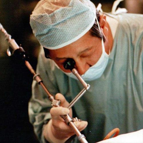 Close-up of Dr. InBae Yoon wearing a surgical gown, cap, and gloves, using a laparoscopic surgical tool. The patient is not visible in the photo.