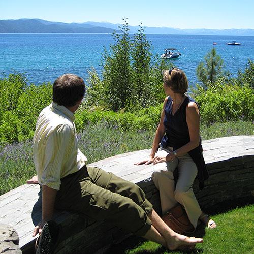 A man and a woman seated on a low wall look out at Lake Tahoe