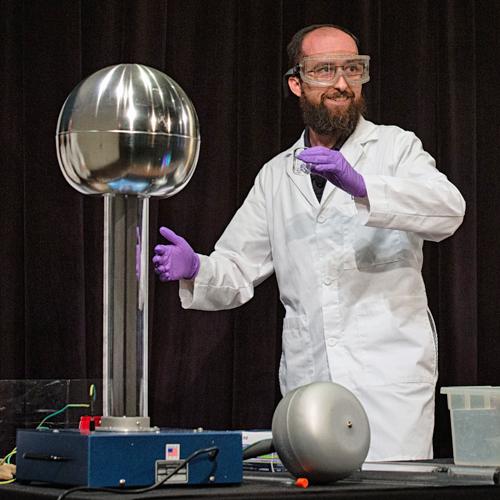 Man in a lab coat and safety goggles about to demonstrate a Van de Graaf generator