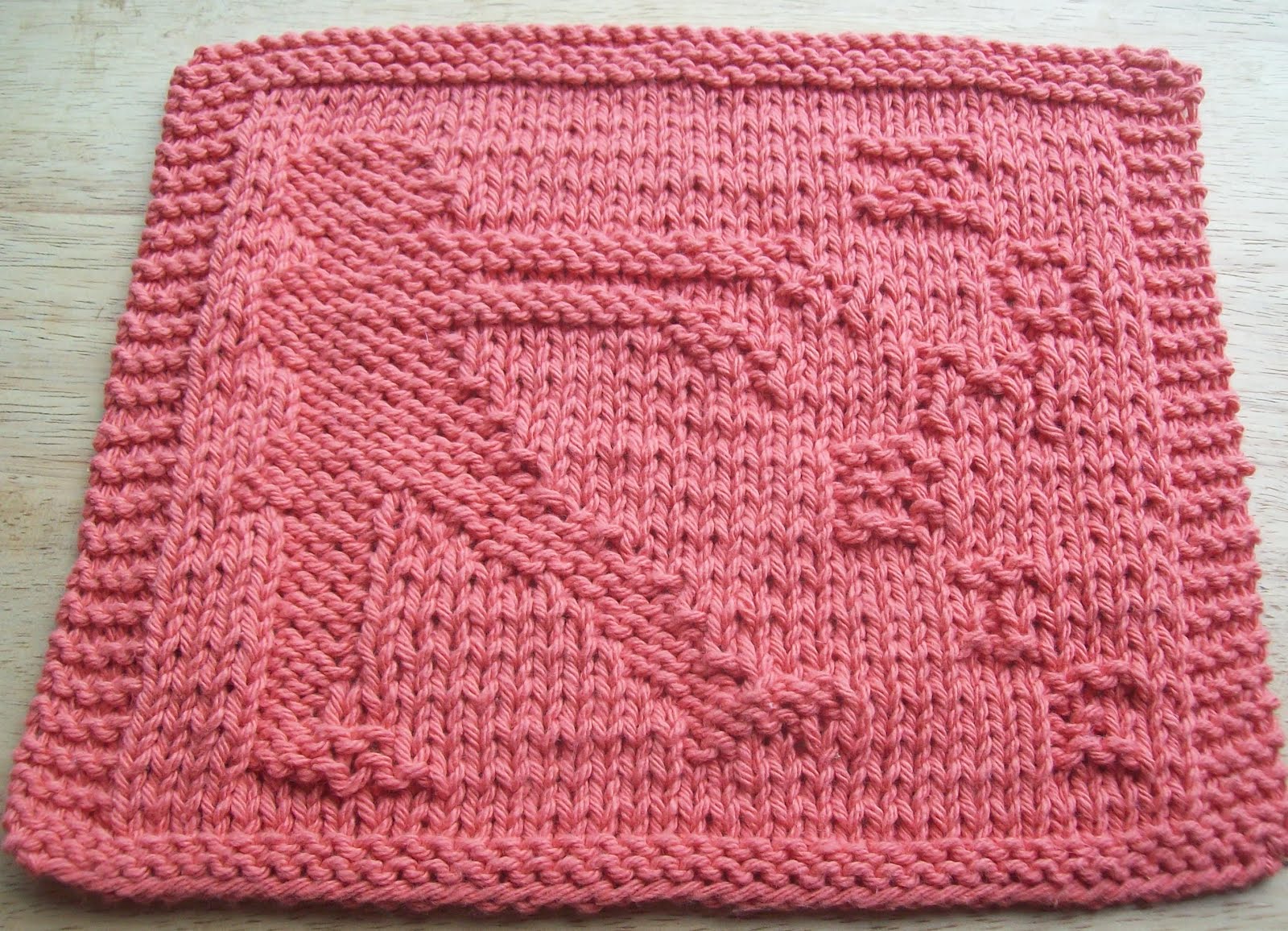 A pink knitted dishcloth incorporating a zombie into the design.